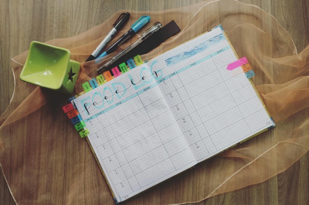 Open food log planner with colorful tabs and pens on a wooden desk, perfect for meal tracking.