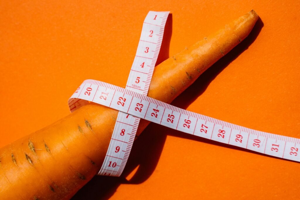 Close-up shot of a carrot wrapped with a measuring tape on a vibrant orange background, symbolizing healthy eating.