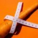 Close-up shot of a carrot wrapped with a measuring tape on a vibrant orange background, symbolizing healthy eating.